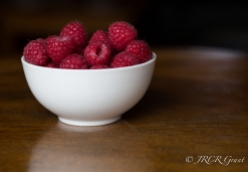 A bowl of raspberries atop a polished wooden table