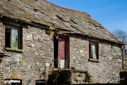 Large roof slates gradually slip from an old barn